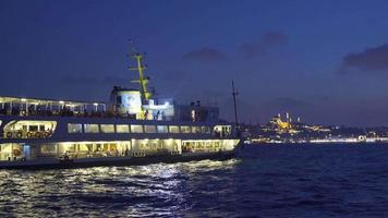 Ferry in Istanbul. The mosque is visible in the background. The ferry sails at night on the Istanbul estuary. There are passengers inside. City view from the sea. video