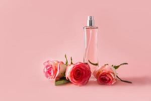 un elegante transparente botella de un cosmético perfume producto en un rosado antecedentes con un réplica de el espacio y Tres Fresco rosas. foto