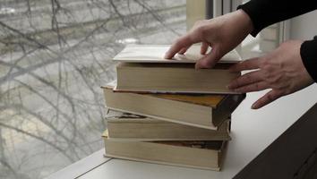 A person reading books near the window. Hands turns over book page. photo