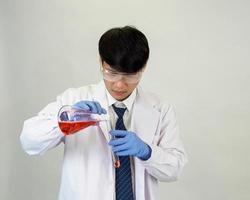 asiático hombre estudiante científico o médico en reactivo mezcla laboratorio en un Ciencias investigación laboratorio con prueba tubos de varios tamaños en el piso en laboratorio química laboratorio blanco antecedentes. foto