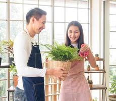 portrait lovers handsome young man Pretty Asian woman wearing white t-shirt. and apron joking having fun help arrange plant and water plants in small pots In the room arranged plants with love happily photo