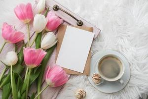 A bouquet of tulips, cup of coffee and mock up blank white paper card for text. Flat lay, top view. Place for text. Greeting card photo