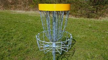 Disc Golf basket. Frisbee golf is sport and hobbie in outdoor park. Metal basket with chains for disc game surrounded by vibrant green trees. photo