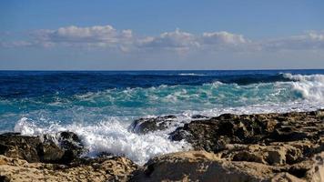 Blue sea wave and white foam and splash. Stone beach on island of Malta, no sandy beach. Summer holiday border frame concept. Tropical island vacation backdrop. Tourist travel banner design template. photo