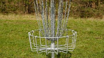 Disc Golf basket. Frisbee golf is sport and hobbie in outdoor park. Metal basket with chains for disc game surrounded by vibrant green trees. photo