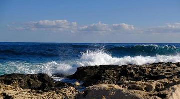 Blue sea wave and white foam and splash. Stone beach on island of Malta, no sandy beach. Summer holiday border frame concept. Tropical island vacation backdrop. Tourist travel banner design template. photo