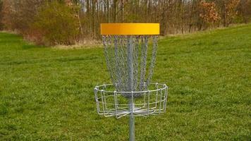 Disc Golf basket. Frisbee golf is sport and hobbie in outdoor park. Metal basket with chains for disc game surrounded by vibrant green trees. photo