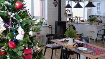 Woman lights a hearth in festive interior of home is decorated for Christmas and New Year in loft style with black stove, fireplace, Christmas tree. burning wood, cozy and heating of home video