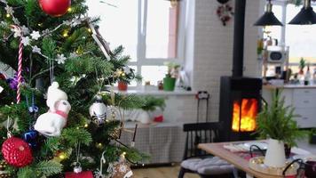 Festive interior of house is decorated for Christmas and New Year in loft style with black stove, fireplace, Christmas tree. Warm studio room with set table, burning wood, cozy and heating of home video