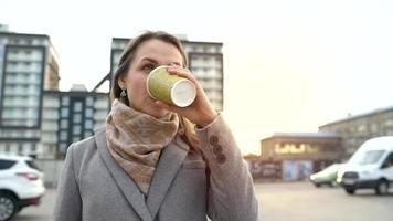 porträtt av en kvinna på en stad bakgrund. kvinna drycker kaffe, vänder runt om och lämna video