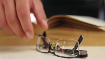 estudiante vistiendo lentes y leyendo libro, estudiante hojeada paginas de libro a escritorio y empieza a estudiar, selectivo atención video