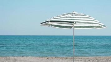 sole ombrello su mare spiaggia, sole ombrello su sabbia ondeggiante a partire dal vento su un' soleggiato e ventoso estate giorno, selettivo messa a fuoco video