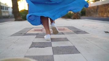 poten van een vrouw in een mooi blauw jurk rennen langs de palm Laan. hoed valt naar de grond. dramatisch langzaam beweging video
