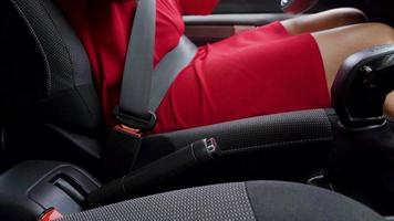 Woman in red dress fastening car safety seat belt while sitting inside of vehicle before driving video