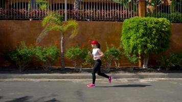 donna corre giù il strada tra il palma alberi. salutare attivo stile di vita video