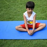 asiático inteligente niño haciendo yoga actitud en el sociedad parque exterior, para niños yoga pose. el pequeño chico haciendo yoga ejercicio. foto