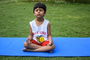 asiático inteligente niño haciendo yoga actitud en el sociedad parque exterior, para niños yoga pose. el pequeño chico haciendo yoga ejercicio. foto