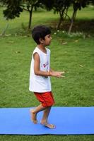 asiático inteligente niño haciendo yoga actitud en el sociedad parque exterior, para niños yoga pose. el pequeño chico haciendo yoga ejercicio. foto