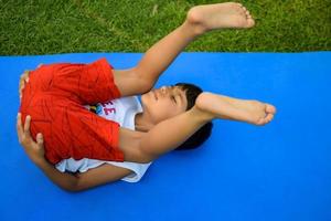 asiático inteligente niño haciendo yoga actitud en el sociedad parque exterior, para niños yoga pose. el pequeño chico haciendo yoga ejercicio. foto