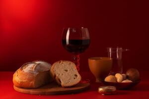 Communion still life with bread, wine, and cup on red background. photo