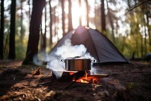 A tent in the forest in the summer by a fire with a pot from which steam comes from food. . photo