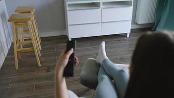 Woman is sitting in a chair, watching TV with a green screen, switching channels with a remote control. Chroma key video