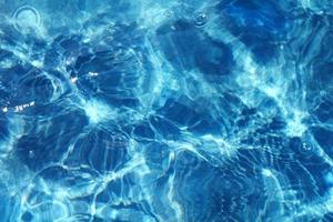 Azure rippled water surface of blue swimming pool. Background of water ripple under bright sunny sky with few drops. Full frame texture. Summer holidays, vacations resort concept. photo