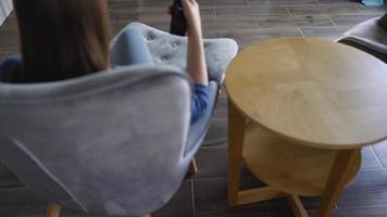 donna è seduta nel un' sedia, Guardando tv con un' verde schermo, commutazione canali con un' a distanza controllo. croma chiave video