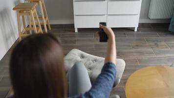 mulher é sentado dentro uma cadeira, assistindo televisão com uma verde tela, trocando canais com uma controlo remoto ao controle. croma chave video