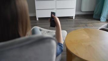 mujer es sentado en un silla, acecho televisión con un verde pantalla, traspuesta canales con un remoto control. croma llave video