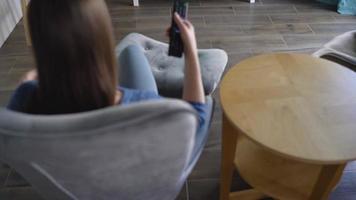 donna è seduta nel un' sedia, Guardando tv con un' verde schermo, commutazione canali con un' a distanza controllo. croma chiave video