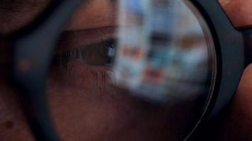 Man in glasses looking on the monitor and surfing Internet. The monitor screen is reflected in the glasses video