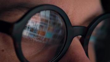 Man in glasses looking on the monitor and surfing Internet. The monitor screen is reflected in the glasses video