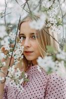 rubia niña en un primavera caminar en el jardín con Cereza flores hembra retrato, de cerca. un niña en un rosado polca punto vestido. foto