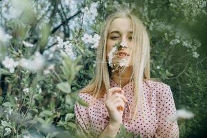 rubia niña en un primavera caminar en el jardín con Cereza flores hembra retrato, de cerca. un niña en un rosado polca punto vestido. foto