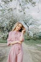 rubia niña en un primavera caminar en el jardín con Cereza flores hembra retrato, de cerca. un niña en un rosado polca punto vestido. foto