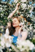 Beautiful young girl in a blue dress in a blooming Apple orchard. Blooming Apple trees with white flowers. photo