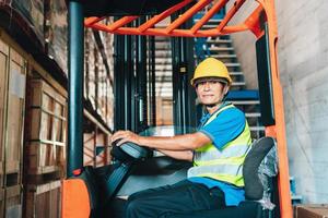 Worker driver asian man in protective safety jumpsuit uniform with yellow hardhat at warehouse forklift loader works photo