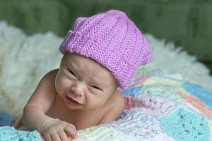 Newborn baby with funny face. Little baby in pink cap is crying. photo