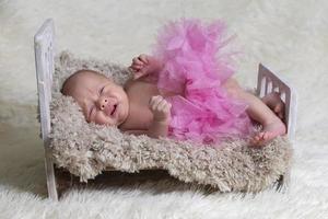 Newborn baby crying in the crib.Baby in a pink skirt on a fur bed. photo