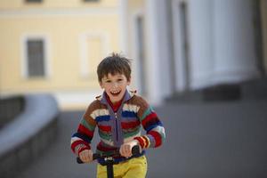 The child is holding the wheel of the scooter. Cheerful boy on a walk in the street. photo