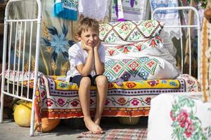 Child Russian or Ukrainian on an old ethnic bed with pillows and bedspreads embroidered with a Slavic pattern. Belarusian boy. photo