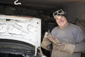 Cheerful male auto mechanic in dirty clothes in the garage. photo