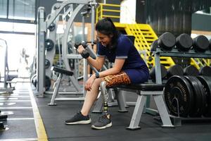 Young female with one prosthetic leg warms up by lifting light weights. Concept of living a woman's life with a prosthetic limb. photo