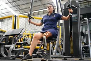 Young female with one prosthetic leg with shoulder exercises with exercise machines to train the muscles in the torso and shoulders, the concept of living a woman's life with a prosthetic leg. photo