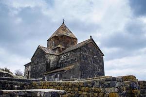 monasterio situado en el apuntalar de lago sevan concepto foto. monasterio complejo debajo dramático primavera cielo. alto calidad imagen para fondo de pantalla foto