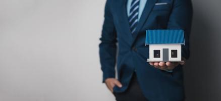 Close up view of young businessman or real estate agent holding a house model as a symbol of property investment. photo