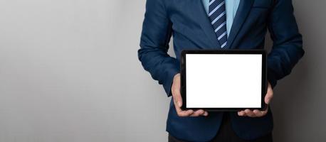 Cropped shot view of young smart businessman holding blank screen tablet while standing against empty wall. photo