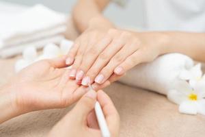 la mujer recibe el servicio de atención de la manicura esteticista profesional en el centro de spa. el salón de belleza de uñas usa una lima de uñas para el tratamiento de acristalamiento. manicurista hace que el cliente de uñas sea hermoso. tratamiento de spa para el cuidado del cuerpo foto