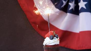 Fourth of july celebration. Sweet cupcake with blueberries and strawberry and sparkler over USA flag background video